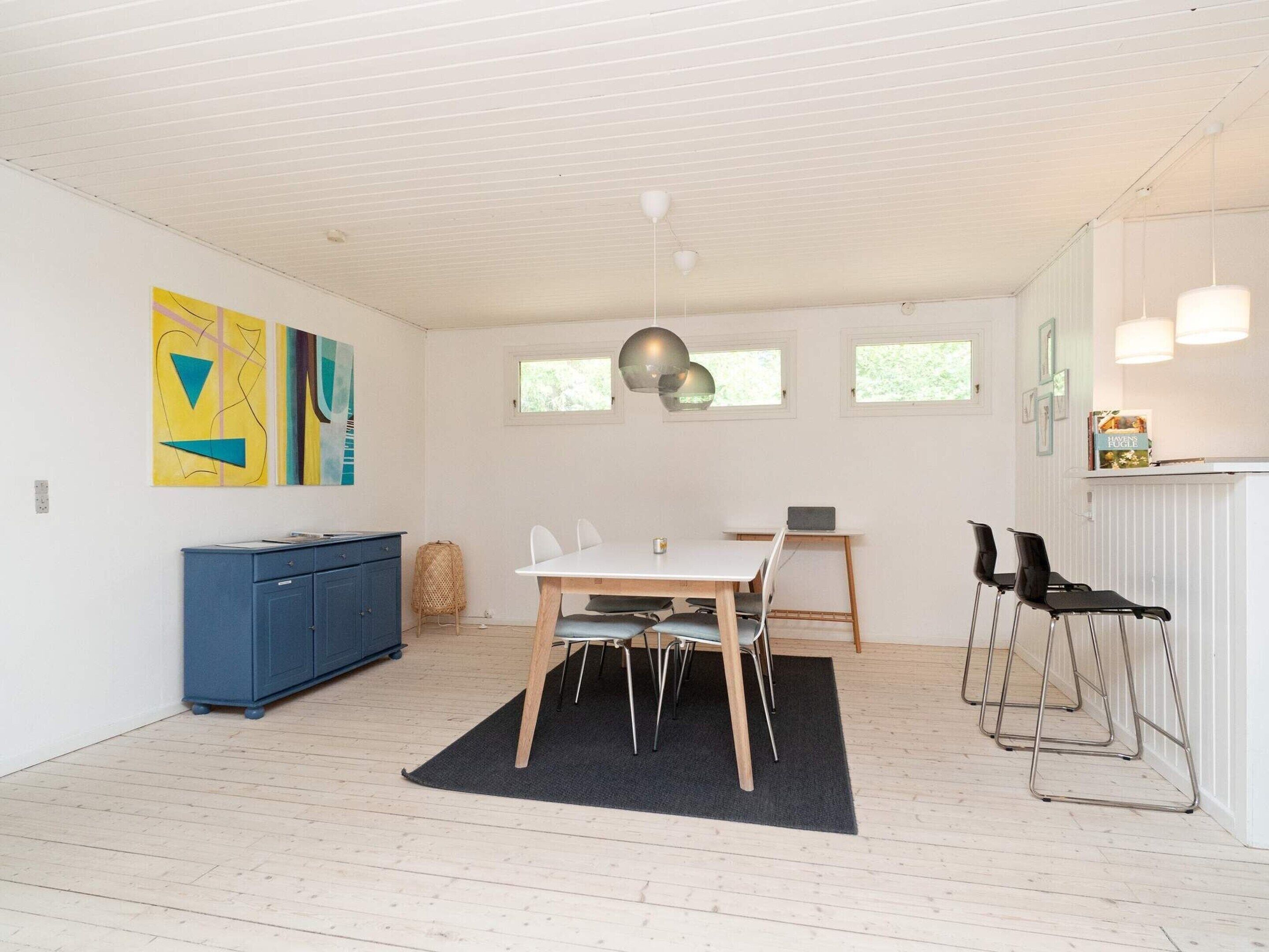Une cuisine moderne avec un plan de travail blanc, un meuble bleu et un coin repas comprenant une table et des chaises.