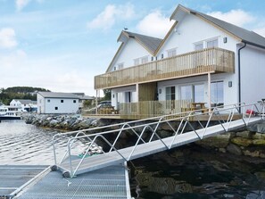 Ein Anwesen am Wasserufer mit einer Holzterrasse, einer Metalltreppe und einem Gebäude mit Balkon.