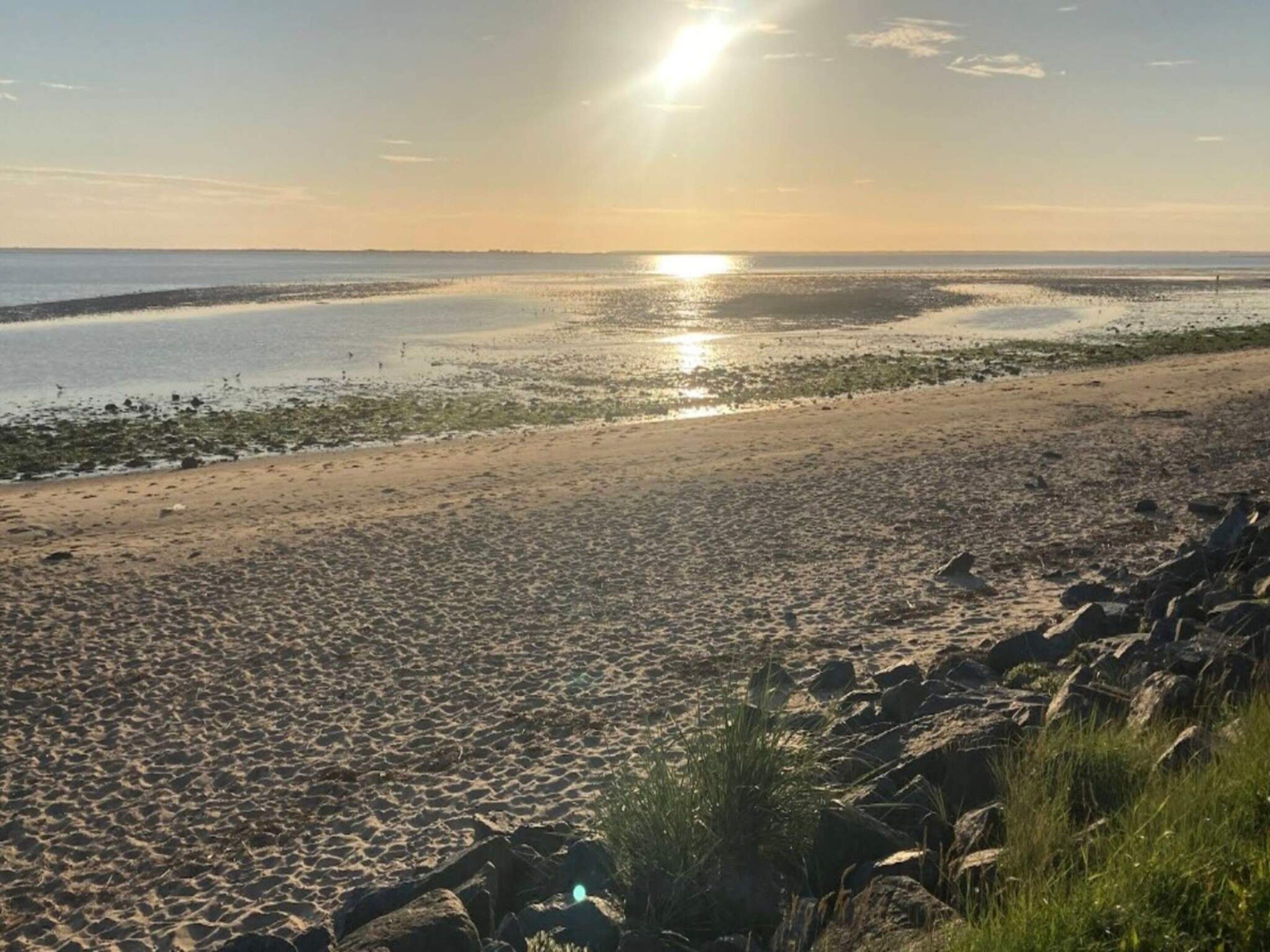 A beach with a rocky shoreline and calm water reflecting the sun.
