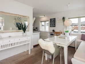 Et moderne køkken med hvide skabe, et stort spejl og et spiseområde med et hvidt bord og stole.