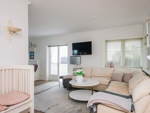 A living room with a sofa, a television mounted on the wall, a small round table, and a window with blinds. - 5 Star Holiday Home in Esbjerg V (Esbjerg)