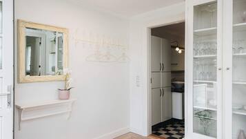 A hallway with a white door, a mirror, a pink vase with flowers, a coat rack, and a cabinet with glass doors.