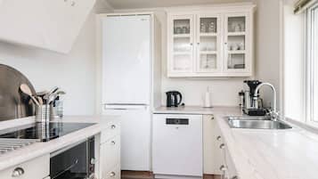 A modern kitchen with white cabinetry, a built-in oven, a dishwasher, and a coffee maker.