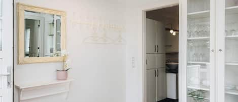 A hallway with a white door, a mirror with an ornate frame, a pink vase with flowers, a coat rack, and a cabinet with glass doors.