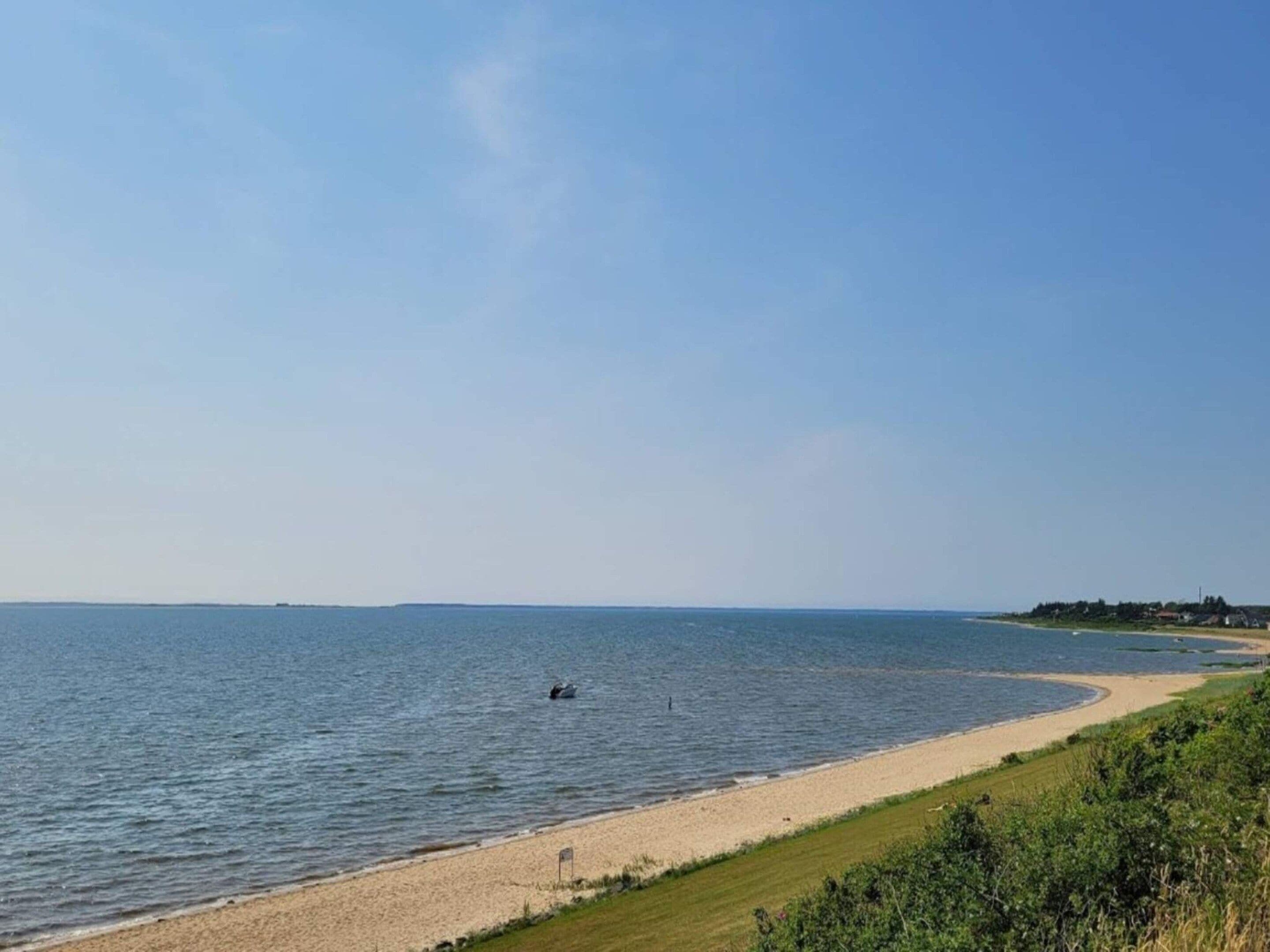 A coastal beach scene with a clear sky, a sandy shore, and a small boat in the water.
