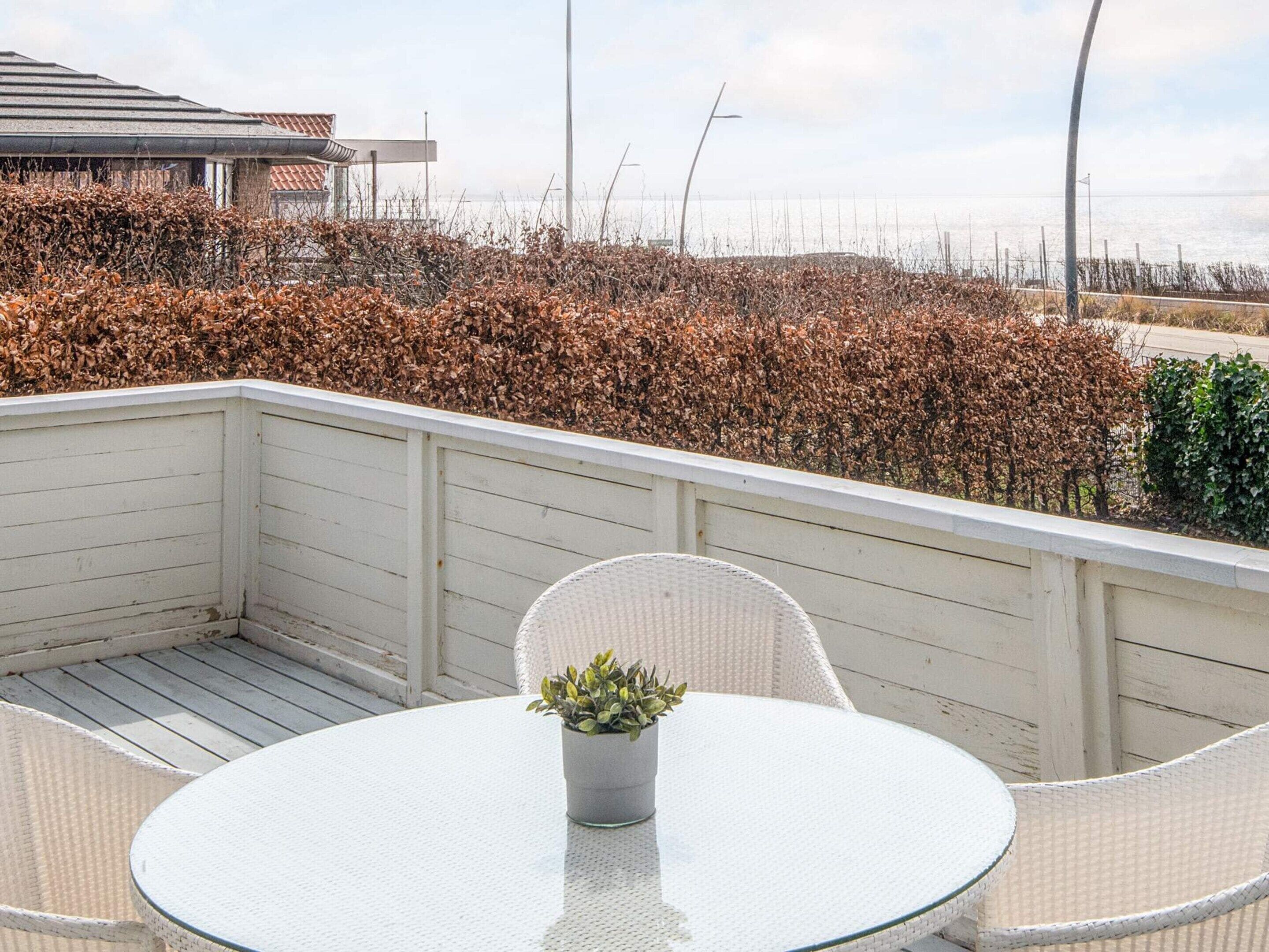 A balcony with a round table and chairs, a potted plant, and a view of the sea and vegetation.