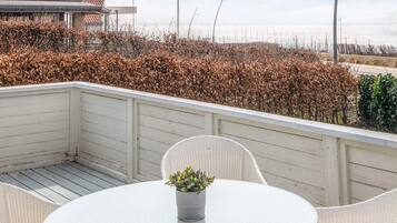 A balcony with a round table and chairs, a potted plant, and a view of the sea and vegetation.
