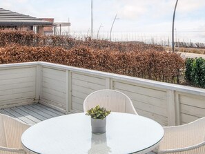 Un balcón con una mesa redonda y sillas, una planta en maceta, y vistas al mar y a la vegetación.