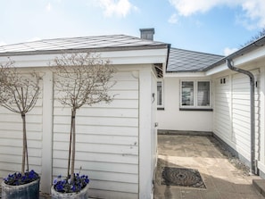 A small, white building with a tiled roof, a window, and a door. There are two potted plants with blue flowers in front. - 5 Star Holiday Home in Esbjerg V (Esbjerg)