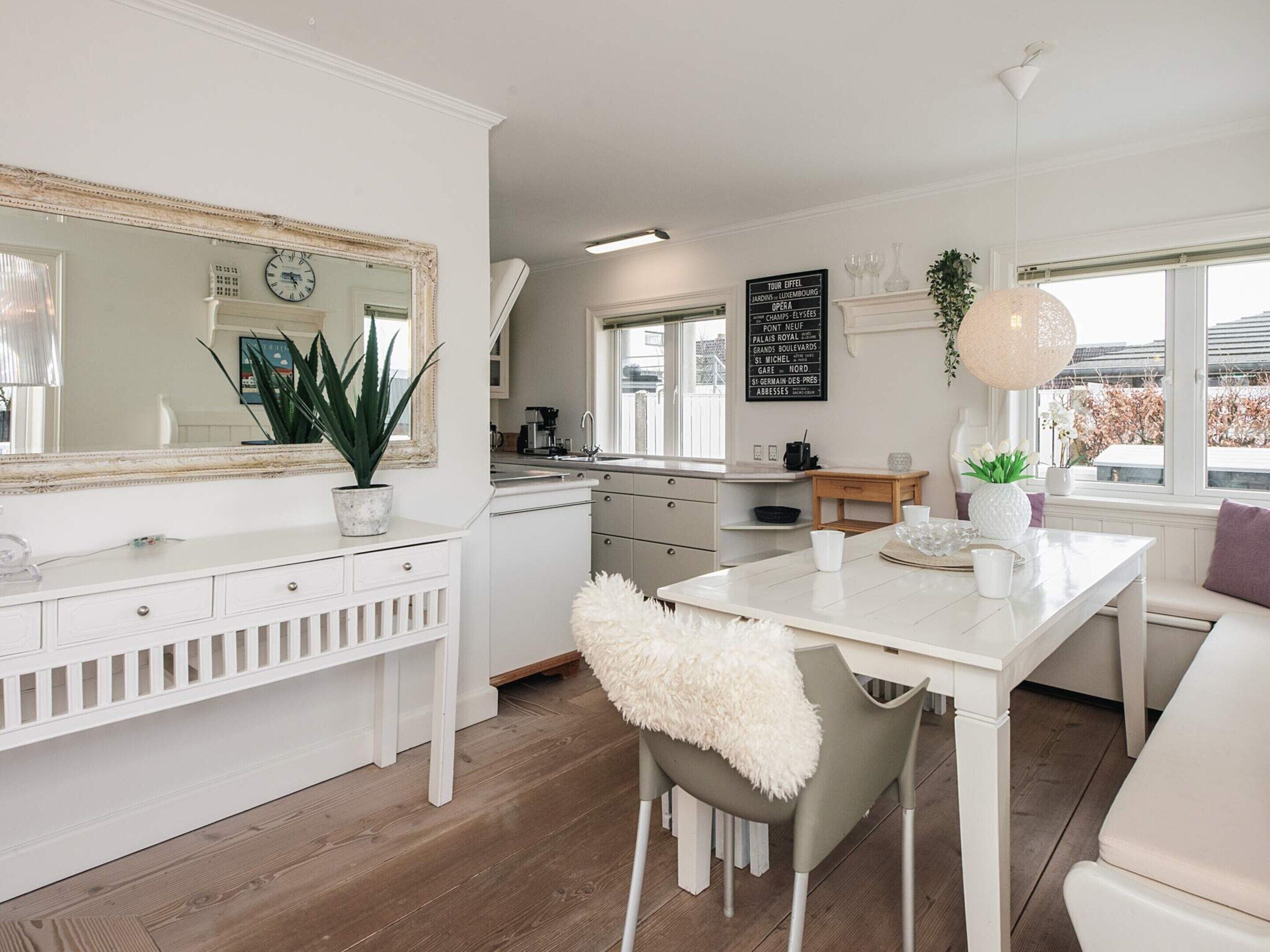 A modern kitchen with white cabinetry, a large mirror, and a dining area with a white table and chairs.