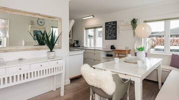 A modern kitchen with white cabinetry, a large mirror, and a dining area with a white table and chairs.