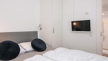 A bedroom with a bed, two black pillows, a white headboard, a wardrobe, and a mounted television.