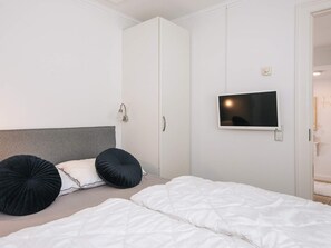 Un dormitorio con una cama, dos almohadas negras, un cabecero blanco, un armario blanco y un televisor montado.