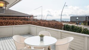 Un espacio de estar al aire libre cubierto, con una mesa redonda y sillas, que ofrece vistas de la costa, un edificio y una carretera.