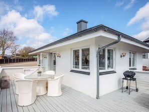 A white building with a covered deck, outdoor seating, and a barbecue grill.