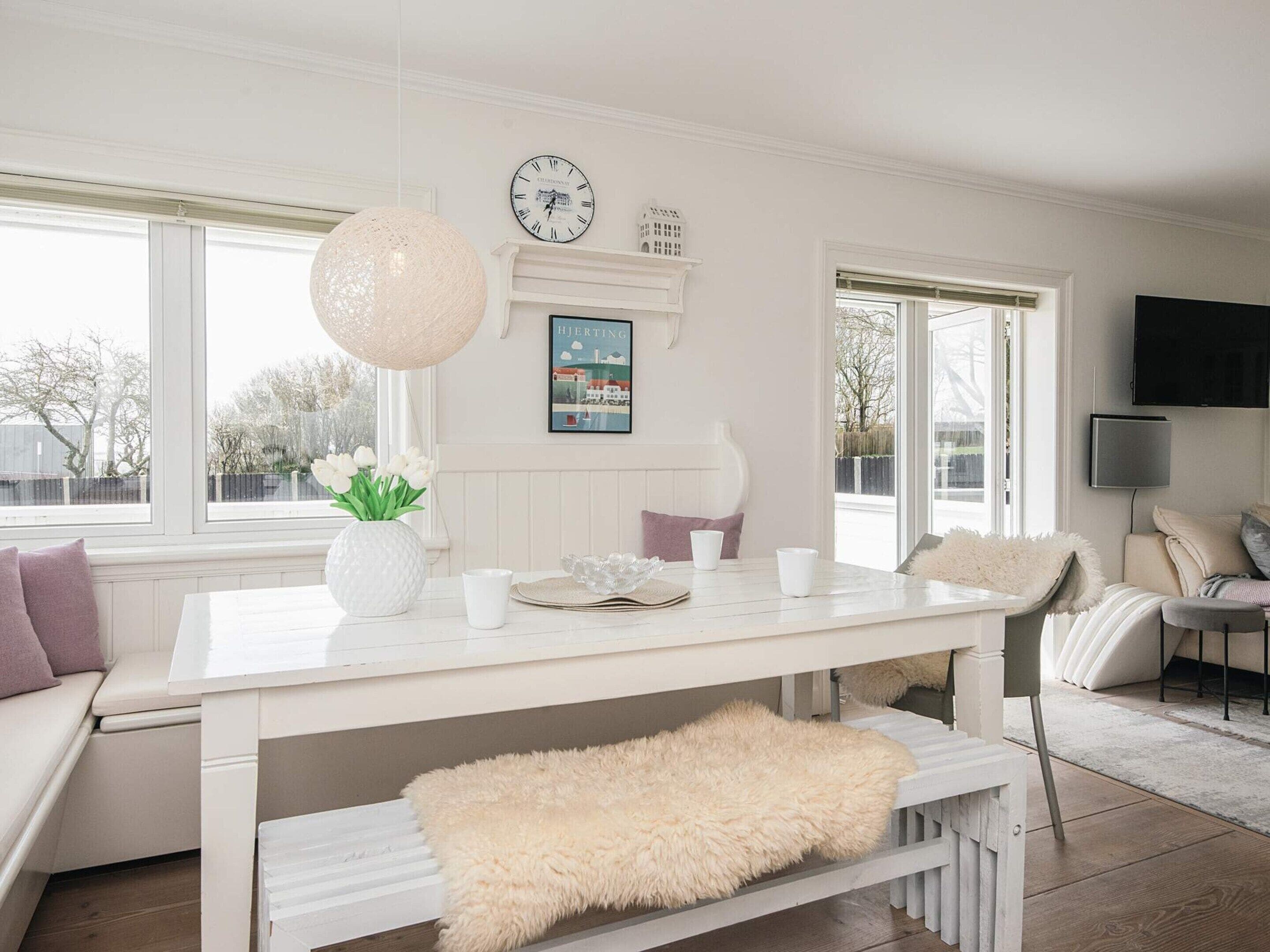 A white dining table with a clock, a vase of flowers, and a framed picture on the wall.