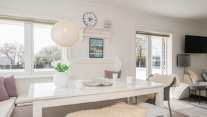 Una mesa de comedor blanca con un reloj, un jarrón de flores y un cuadro en la pared.