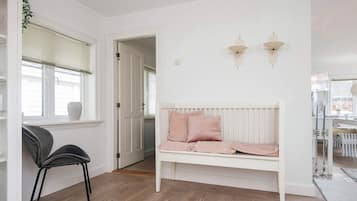 A room with a white bench, a chair, a door, and a window with blinds.