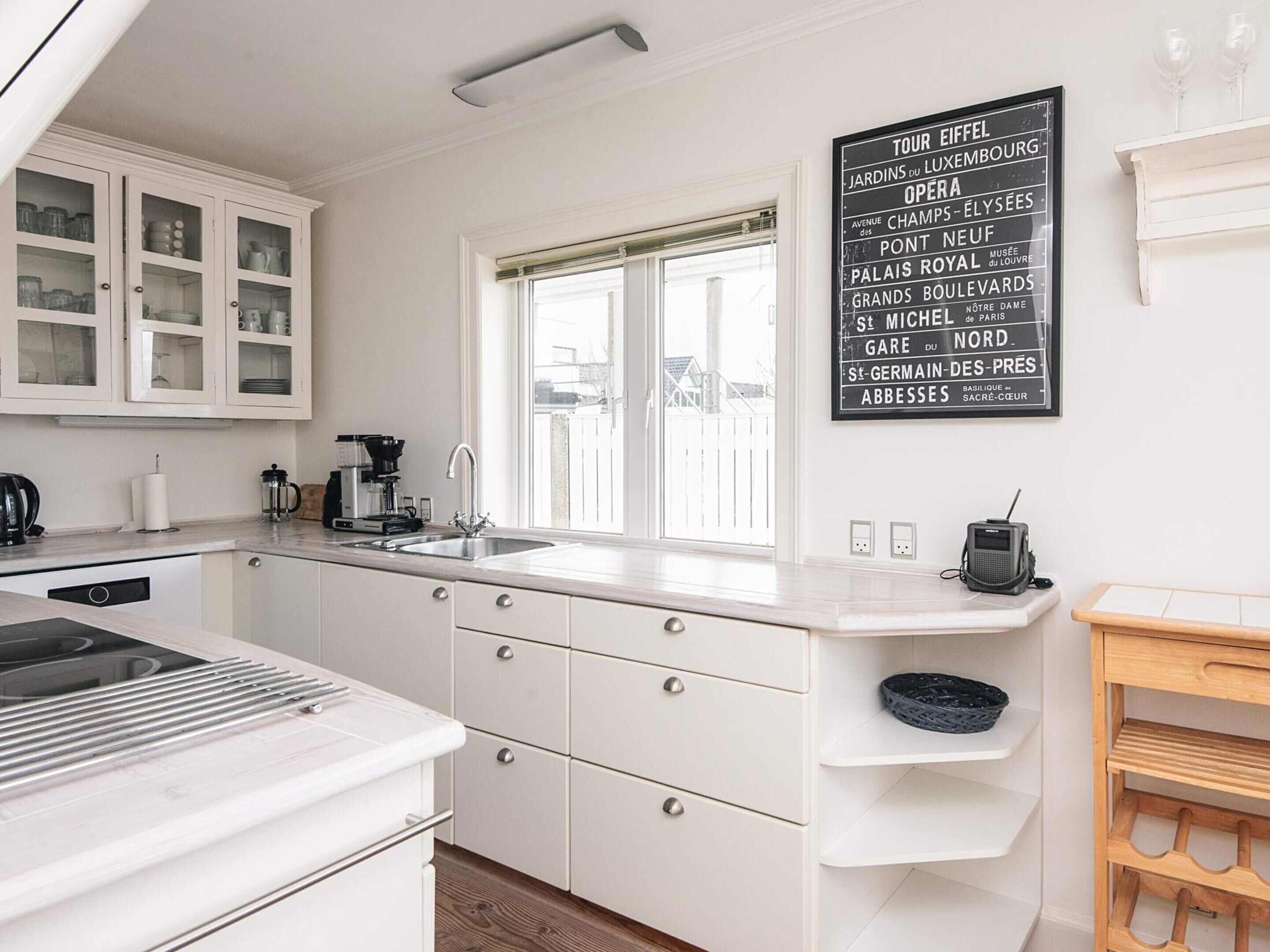 Una cocina moderna con armarios blancos, estufa integrada, un lavamanos y una ventana con persianas.