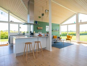 A modern kitchen with a central island, bar stools, and a dining area with a yellow chair. - 4 Star Holiday Home in Otterup (Otterup)