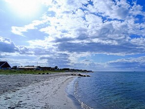 Une plage avec un rivage sablonneux, un ciel dégagé et quelques bâtiments visibles au loin.