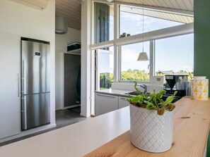 Une cuisine moderne dotée d’un réfrigérateur en acier inoxydable, d’un plan de travail blanc et d’une grande fenêtre donnant sur un paysage verdoyant.