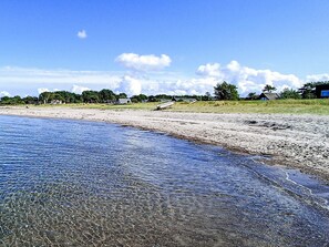Una playa con agua cristalina, orilla de arena y casas al fondo.