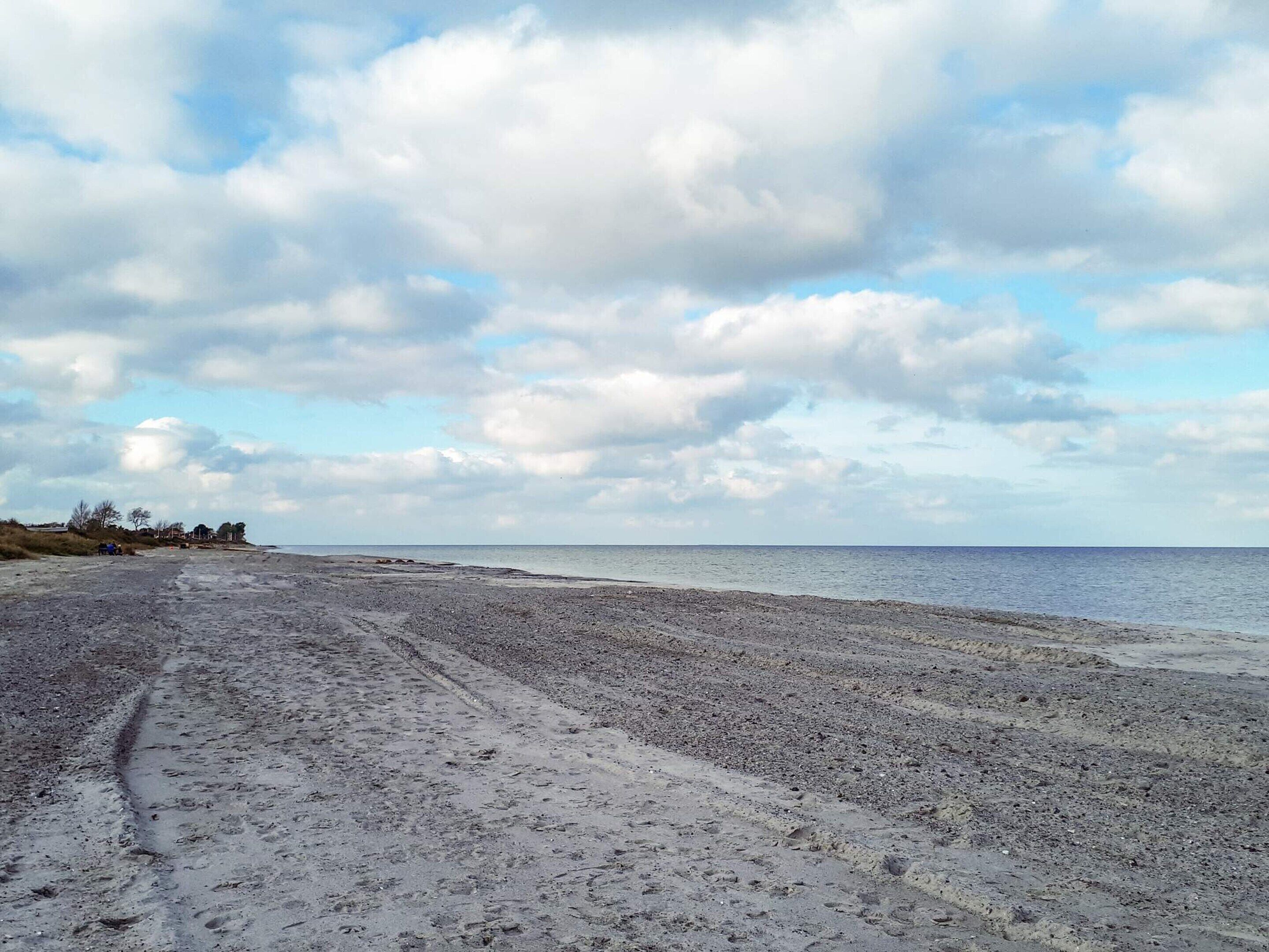A beach with a wide sandy area, a clear sky with clouds, and a calm sea.
