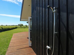 Una terraza de madera que conduce a un edificio negro con sistema de ducha.