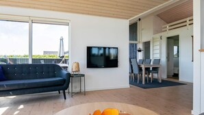 A modern living room with a large TV, a round wooden table, and a blue sofa. - 9 Person Holiday Home in Otterup-by Traum (Otterup)