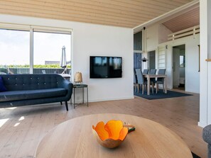 A modern living room with a large TV, a round wooden table, and a blue sofa. - 4 Star Holiday Home in Otterup (Otterup)