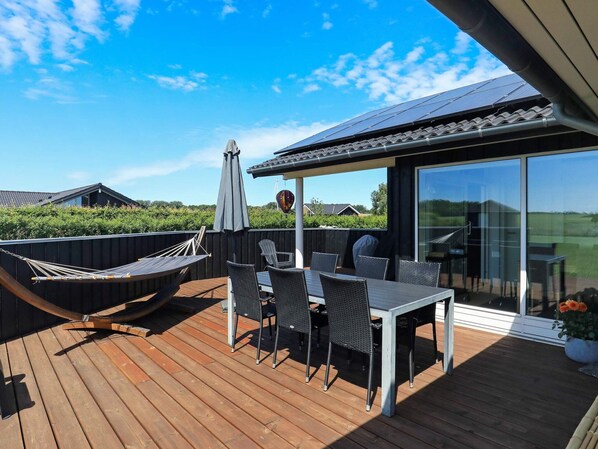 Une terrasse avec une table et des chaises, un hamac et une porte vitrée donnant sur un jardin.