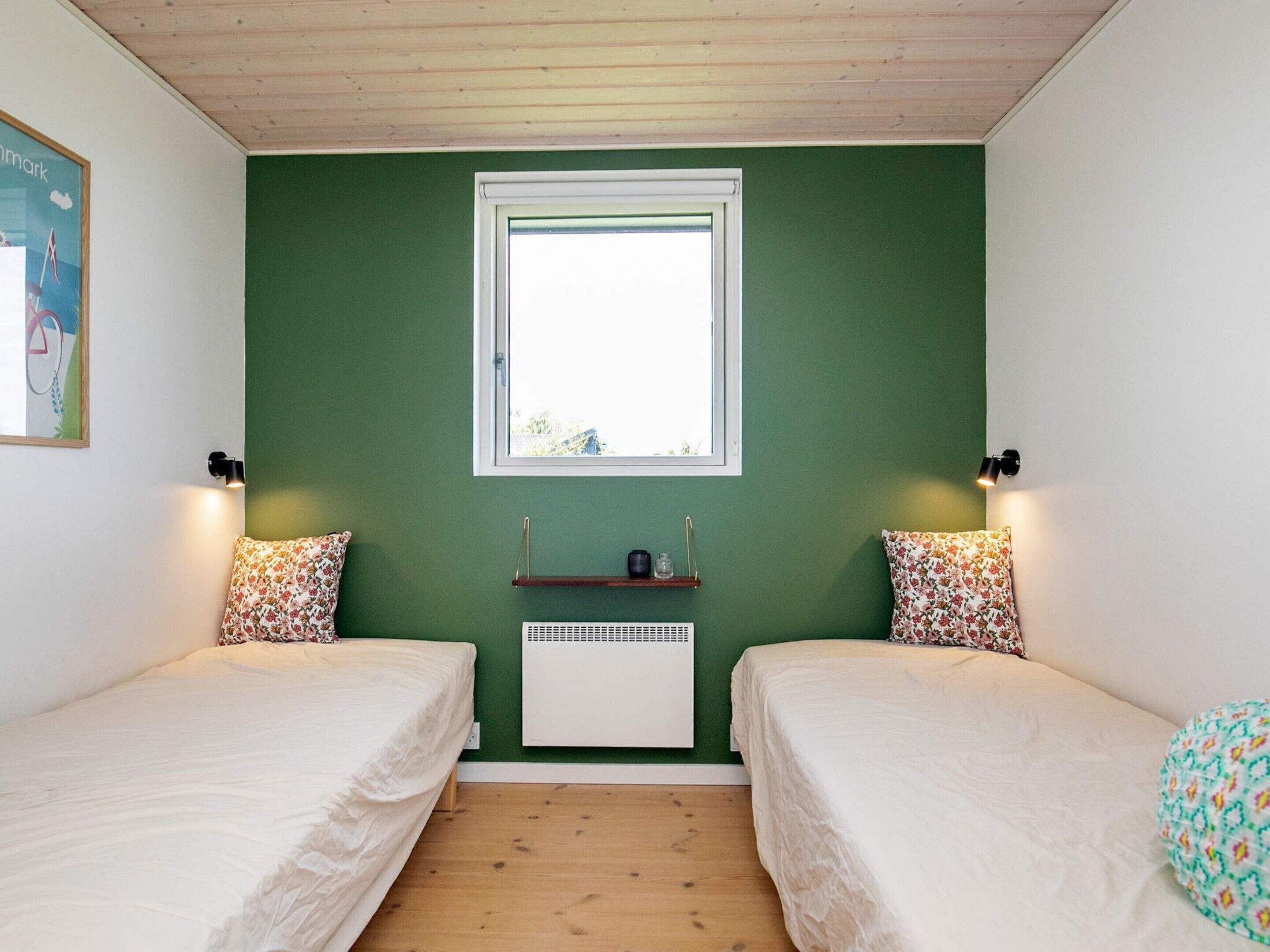 Et værelse med to enkeltsenge, et vindue, en radiator og en lille hylde med genstande.