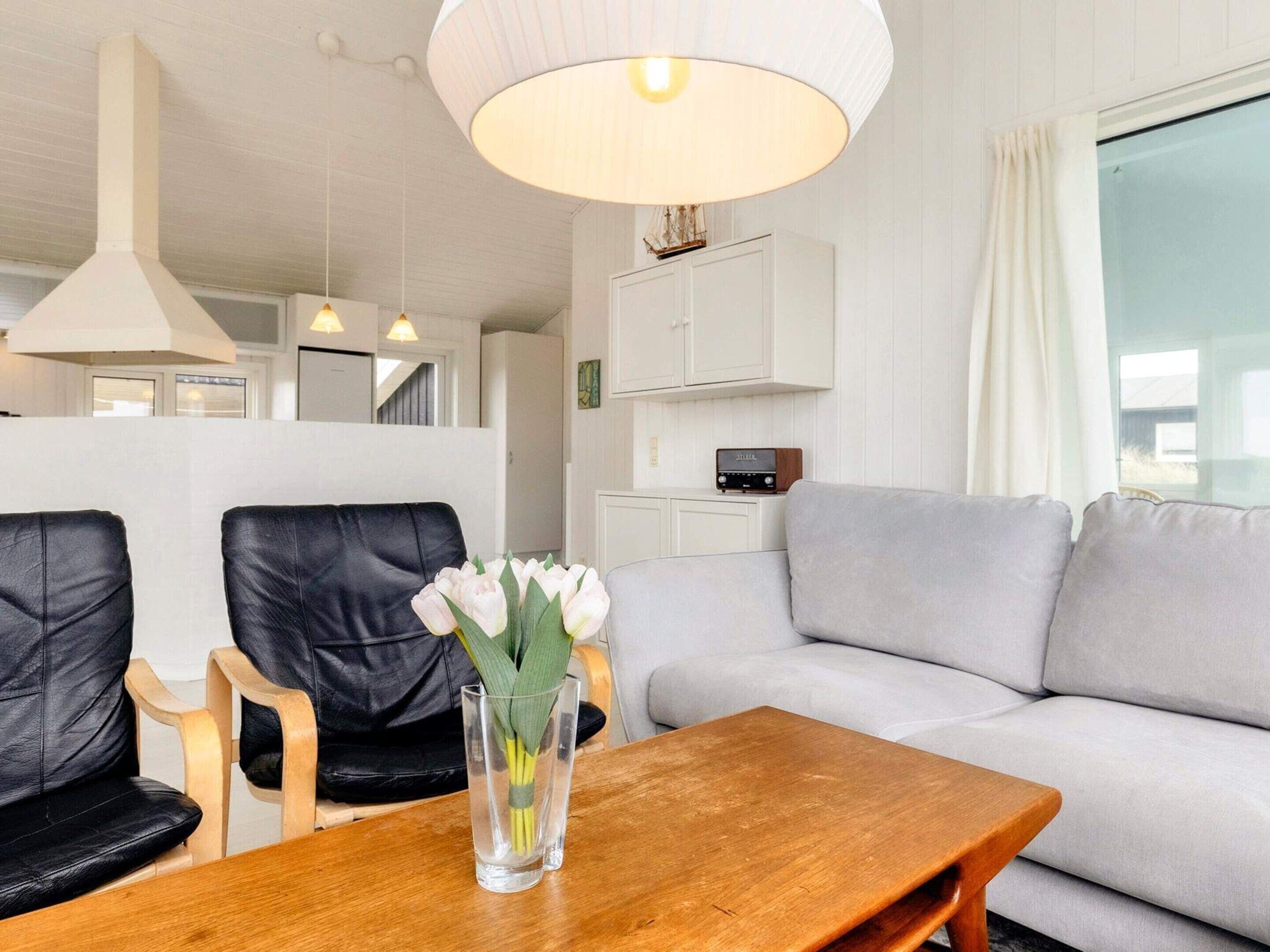 Un salon moderne avec une table en bois, deux fauteuils en cuir noir, un canapé gris et un meuble blanc contenant une radio.