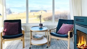 A cozy room with two chairs, a small table, a fireplace, and a large window offering a view of the countryside. - 8 Person Holiday Home in Hjorring (Hjørring)