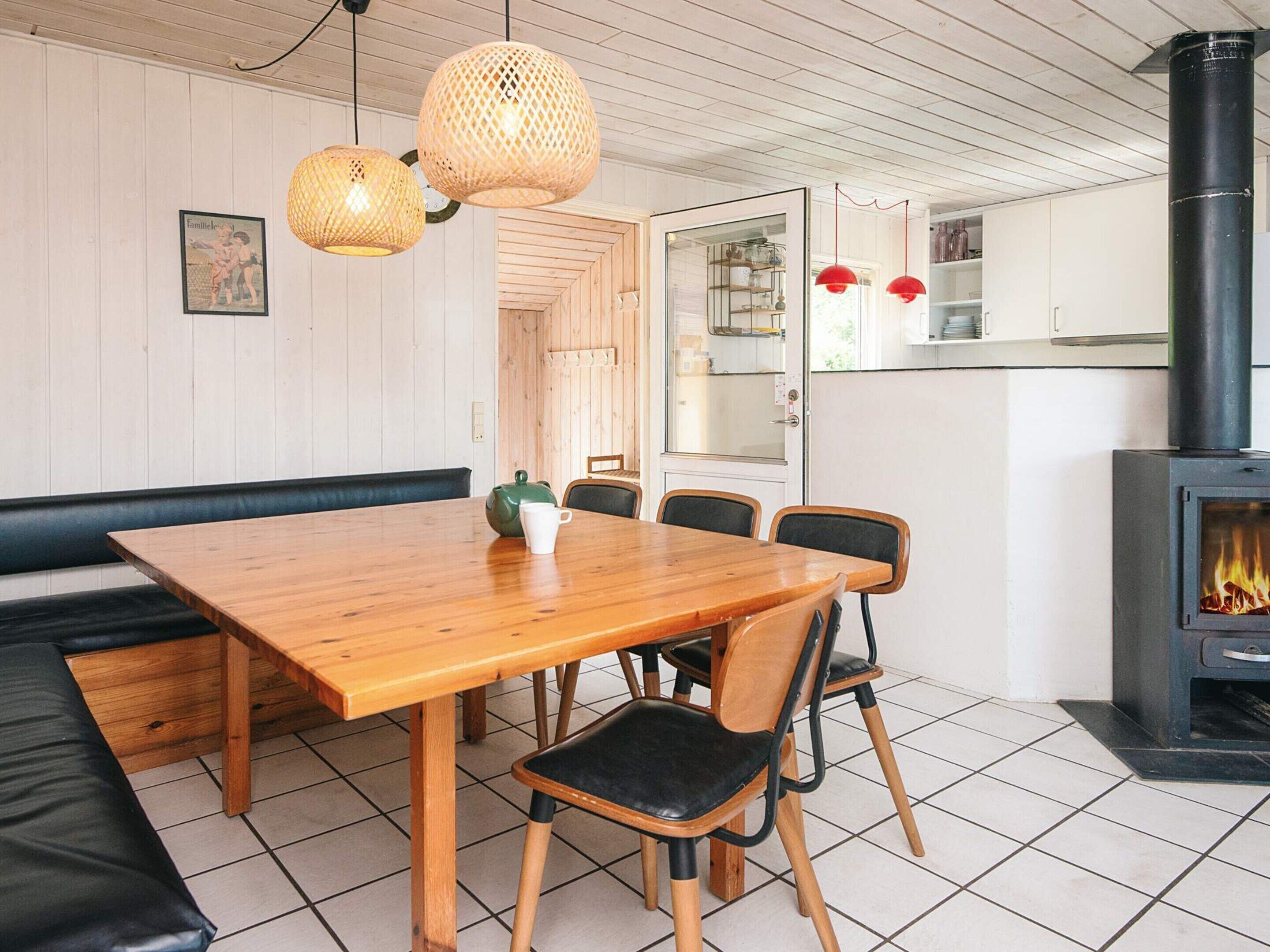 A dining area with a wooden table and chairs, a bench, a fireplace, and hanging wicker lamps.