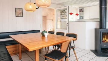 A dining area with a wooden table and chairs, a bench, a fireplace, and hanging wicker lamps.