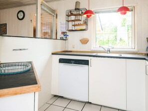 Una cocina con armarios blancos, lavavajillas, ventana con vistas y lámparas colgantes rojas.