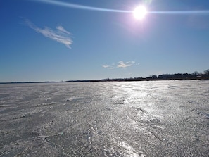 Jäätynyt järvi, kirkas taivas ja kauempana näkyvät puut.
