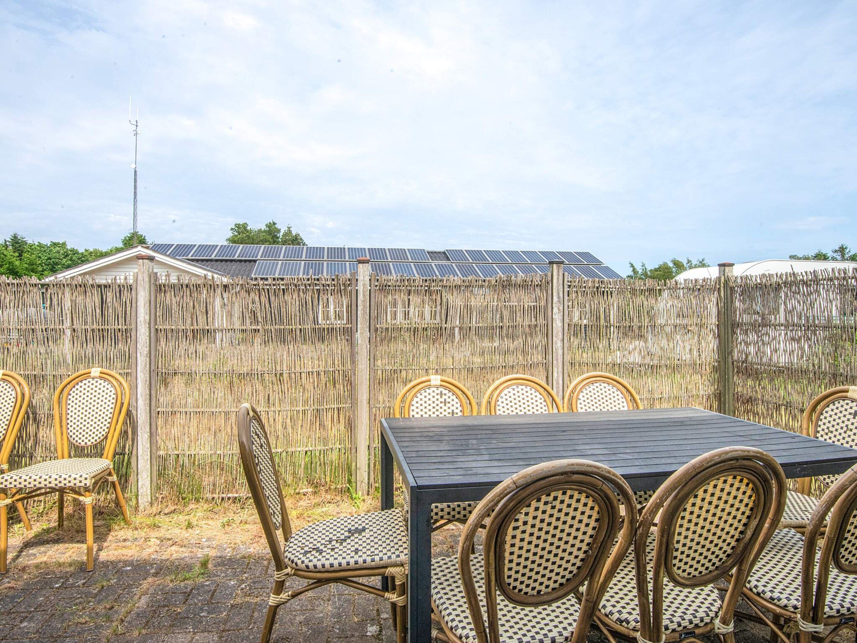 An outdoor patio with a table and chairs, a wooden fence, and solar panels in the background.