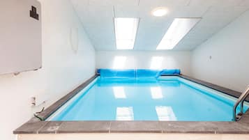 A swimming pool with a tiled edge, a blue pool cover, and a metal ladder.
