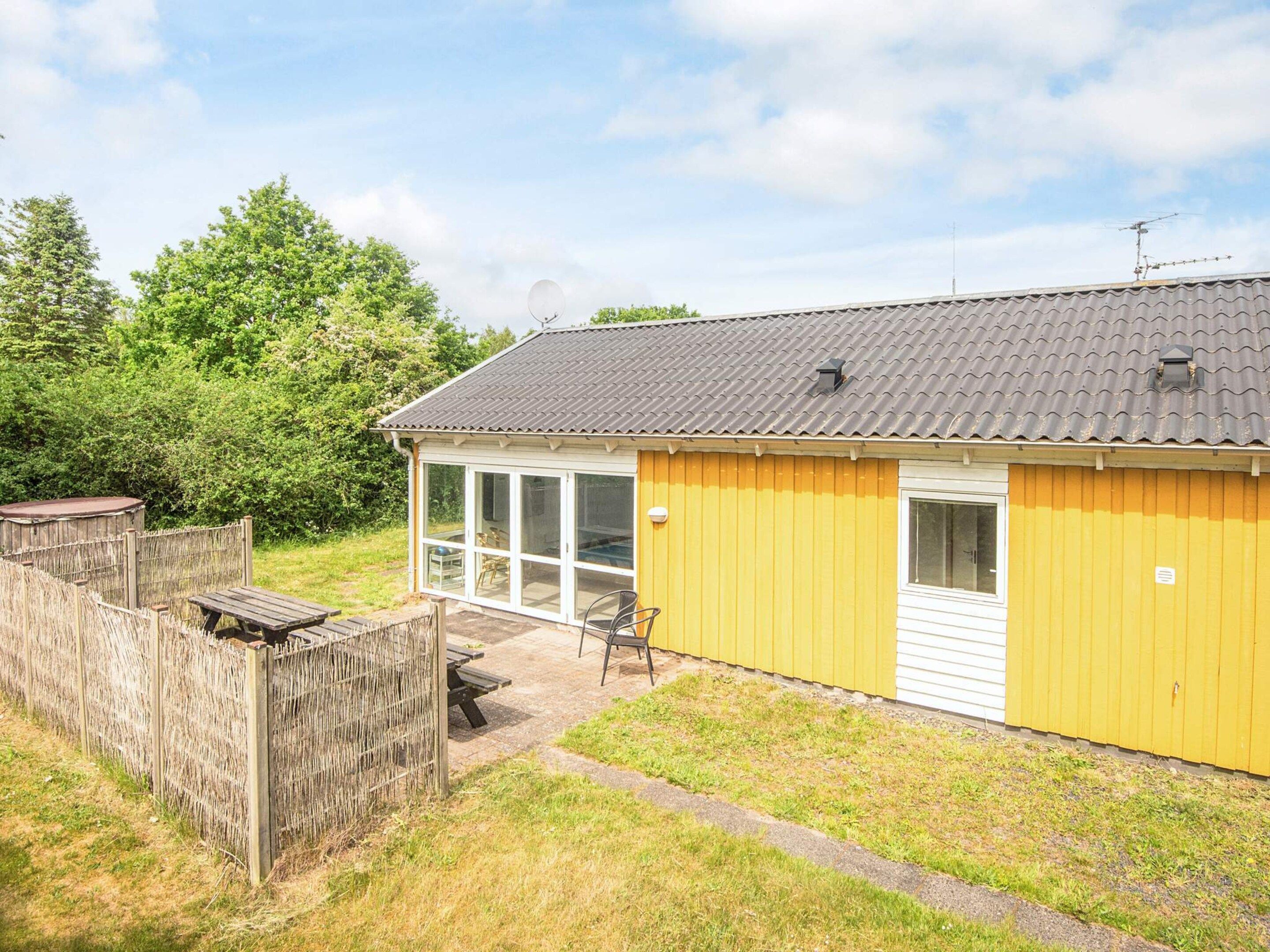 A yellow building with a tiled roof, a fenced outdoor area, and a bench.