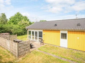 A yellow building with a tiled roof, a fenced outdoor area, and a bench. - 4 Star Holiday Home in Orsted (Ørsted)