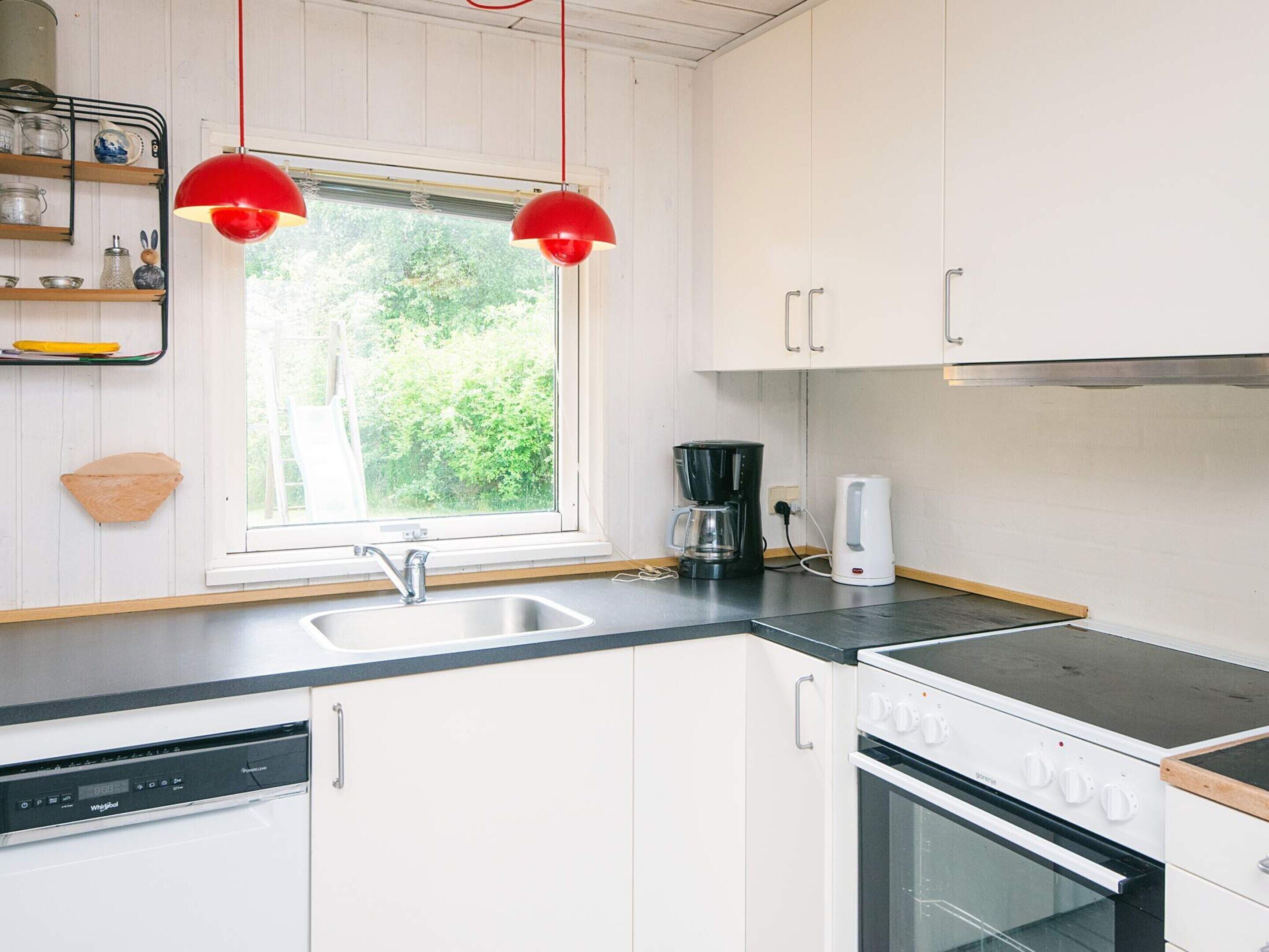 A kitchen with white cabinets, a black countertop, a Bosch dishwasher, a coffee maker, and a stove.