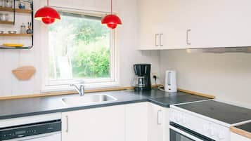 A kitchen with white cabinets, a black countertop, a Bosch dishwasher, a coffee maker, and a stove.