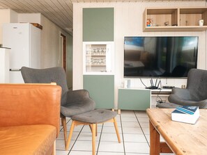 Ein Wohnzimmer mit zwei grauen Sesseln, einem Holztisch, einem Fernseher und einem weißen Kühlschrank.