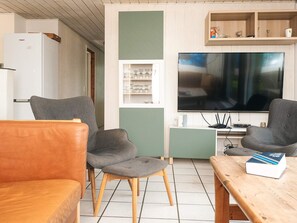 Una sala de estar con dos sillones grises, una mesa de centro de madera, un televisor y un refrigerador blanco.
