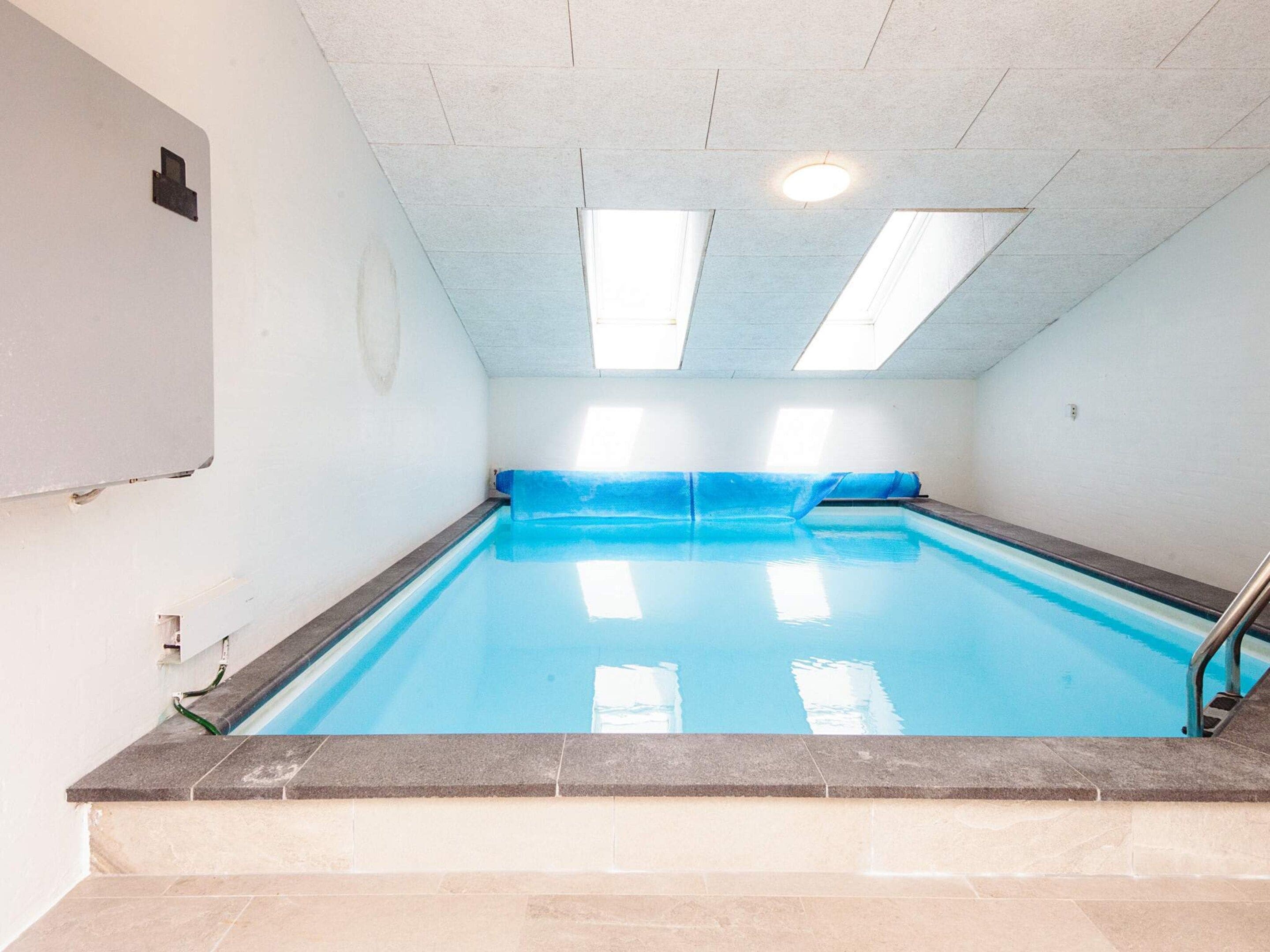 Una piscina con borde de azulejos, una cubierta azul y una escalera de metal.