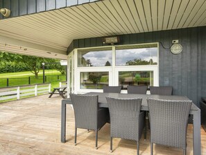 A covered outdoor dining area with a table and chairs, a swing set, and a view of a green landscape. - 7 Person Holiday Home in Hejls (Hejls)