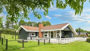 Een tweelaags huis met een overdekte veranda, een bakstenen schoorsteen en een omheinde tuin.